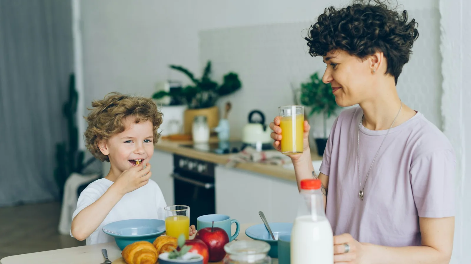 En vuxen och ett barn sitter vid ett frukostbord med juice, frukt och flingor